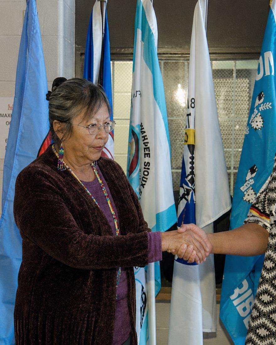 Connie Hopkins meeting with men inside a South Dakota correctional facility, tribal flags behind them